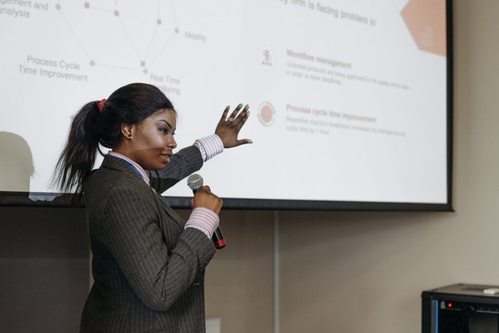 a woman holding a microphone while showing the projector screen