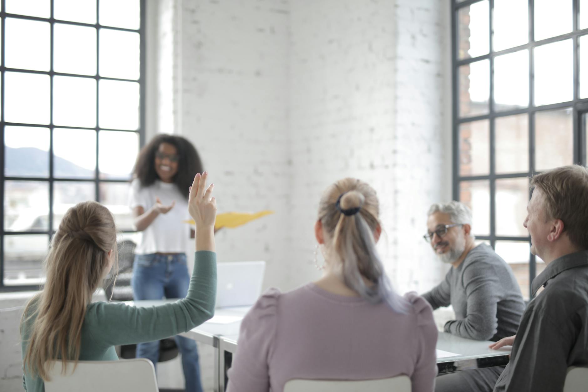 female employee raising hand for asking question at conference in office boardroom